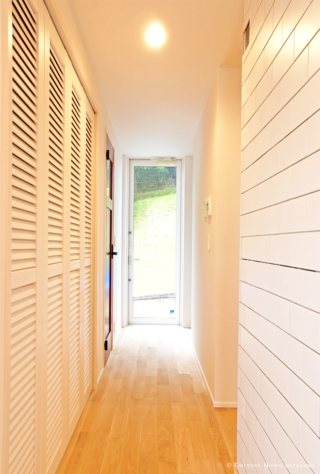 玄関正面の壁を、大開口の勝手口ドアで構成。廊下に間接光を採り込み、風通しも確保。また、木目ルーバータイプの収納扉を採用し、西海岸のビーチテイストを演出。