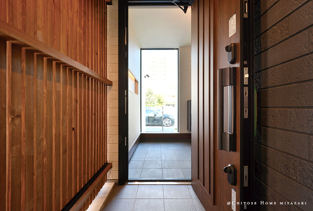 玄関アプローチから玄関ホール内を望む。木製の格子を設けて、ガレージスペースと玄関アプローチをファジーに仕切っている。玄関を格調高い雰囲気に演出。