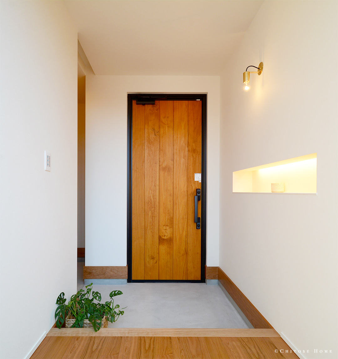 モルタルの床や真鍮の照明など、素材感を活かした玄関ホール。木製パネル貼りの玄関扉とも相まって、経年美化を味わえる、こだわりの詰まった構成に。