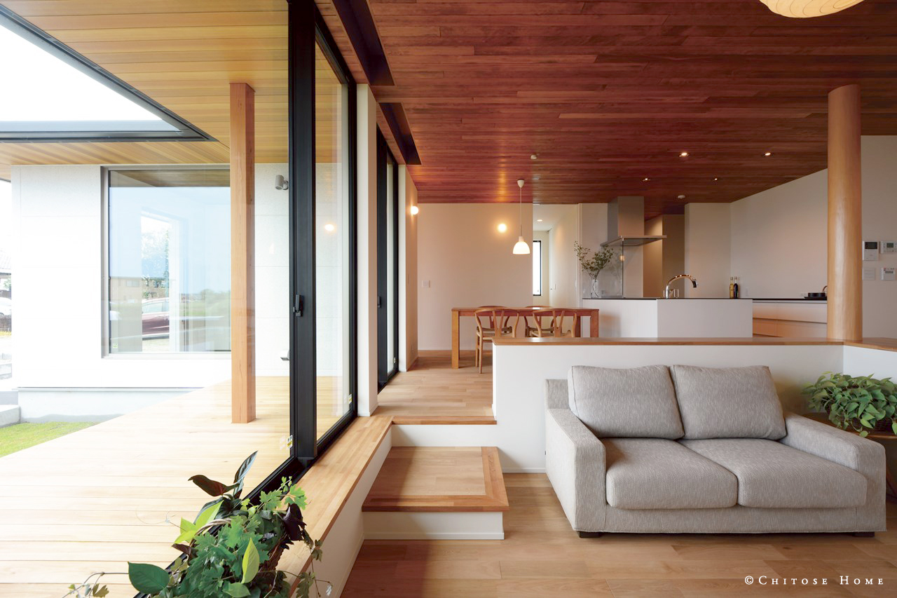高さ２.４ｍのハイサッシを採用した開口部。無垢材の床と天井面の板張り仕上げで、ウチとソトのゆるやかな繋がりを演出。天井に素材感を持たせることで、より水平方向の抜けを強調した空間を構成する。