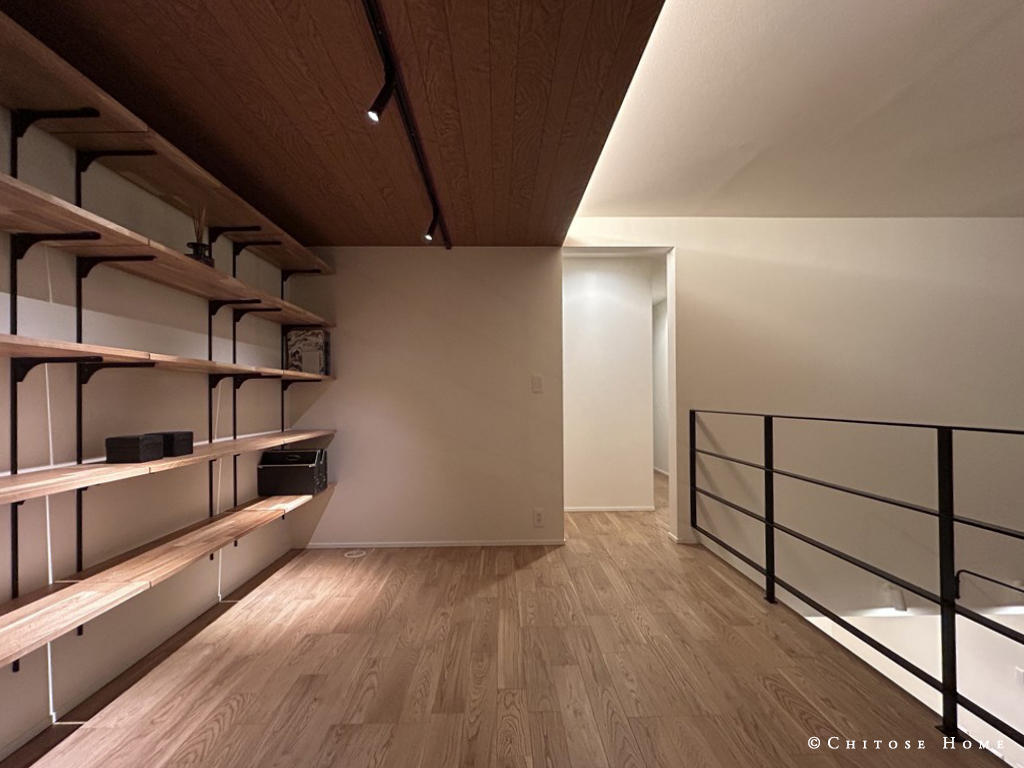 吹き抜けに面した２階ライブラリースペース。下がり天井に仕込んだ間接照明やオープン手摺を採用し、１階との空間の連続性を強める。オークの無垢材を使用した、上質な素材感のある本棚。