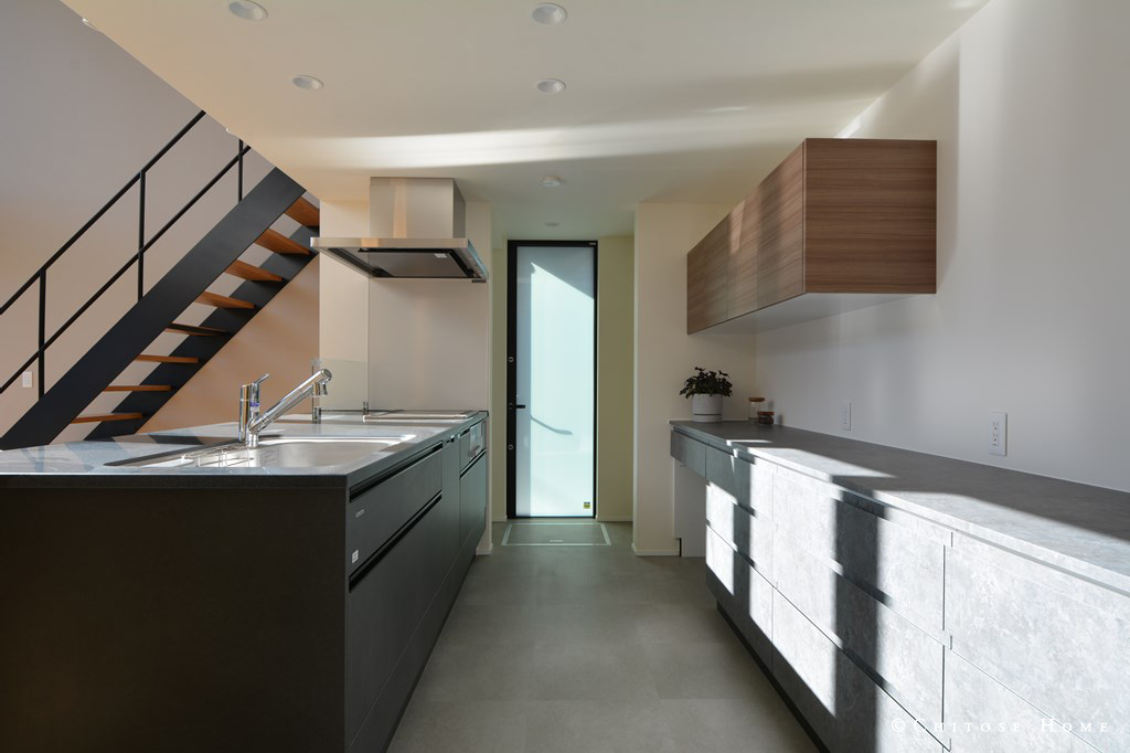 勝手口扉の高さと天井高を揃える。幅や高さのバランスを考慮して吊戸棚を配置する。タイル敷きとキッチンの色彩のトーンを合わせたコーディネート。