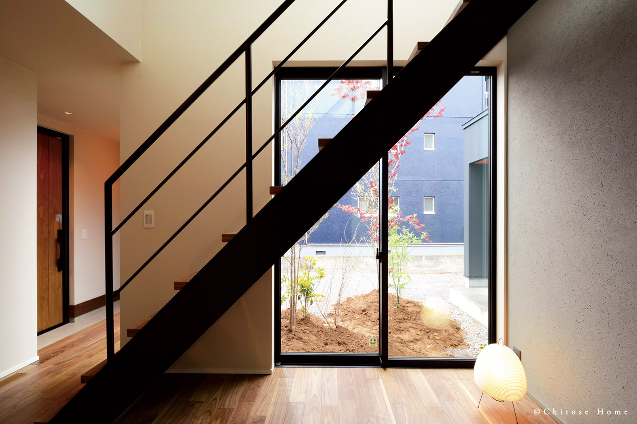 塗り壁とウォルナットの床材の風合いが美しいインテリア空間。オープン階段横に窓を設え、逆光で階段のシルエットを美しく浮き彫りにする。