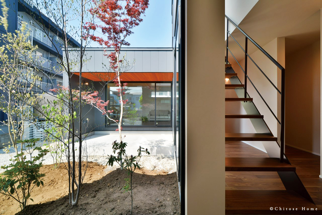 オープン階段のある玄関ホール内の大型FIX窓から中庭を望む。雑木の自然な風合いを、室内に採り込む。