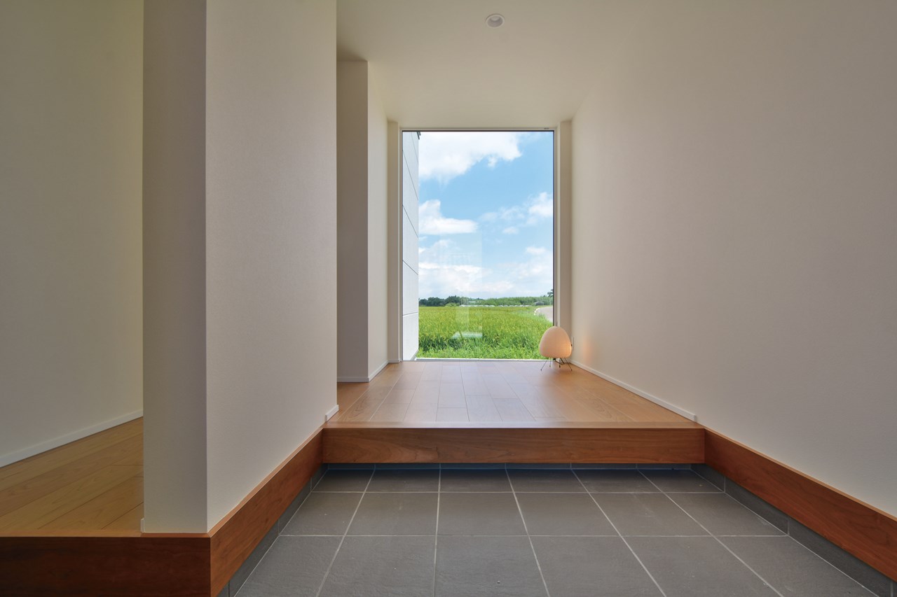 土間収納のある玄関ホールには、正面の壁に床から天井までの大型FIX窓を設えた。水平方向の拡がり感を演出し、田園風景の爽やかな雰囲気を玄関に採り込む。
