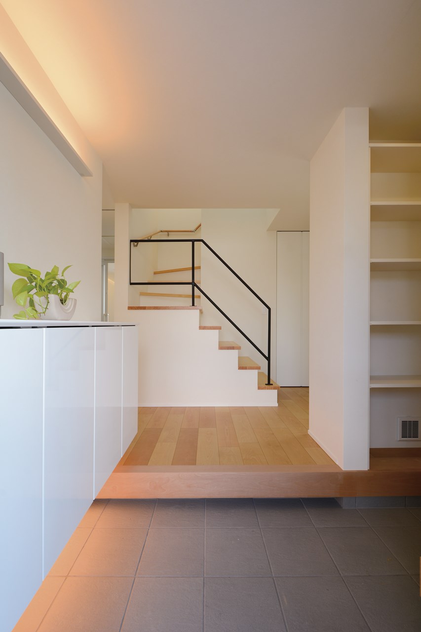 階段上部の窓からスチール手摺の階段越しに、北側窓ならではの自然光を採り込む。子育て世帯ならではの多い荷物をシューズクロークや階段下収納に納めて、すっきりとした上質感のある玄関ホールに演出。