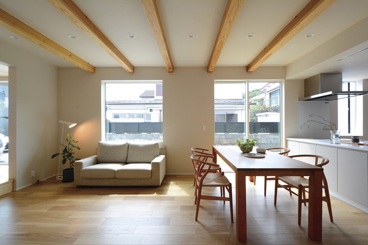ソファの背もたれ側の壁の大型スクエア窓や、ダイニングの掃き出し窓からLDKに光を採り込む。構造材の見出し梁とオーク材の床のトーンを揃えて、自然な風合いで整えたインテリア構成。