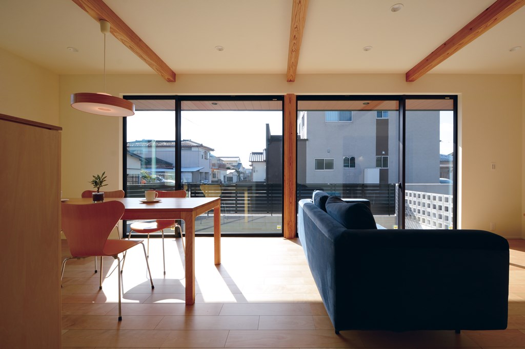 南面に２.５ｍ幅の大開口窓を2連で設え、深い軒のあるタイルデッキを通して外と緩やかにつながるリビング空間。冬の柔らかな陽光を採り込み、ダイニングやソファ周りに心地良い陽だまりをつくる。ご家族がゆったりとくつろげる環境に整える。