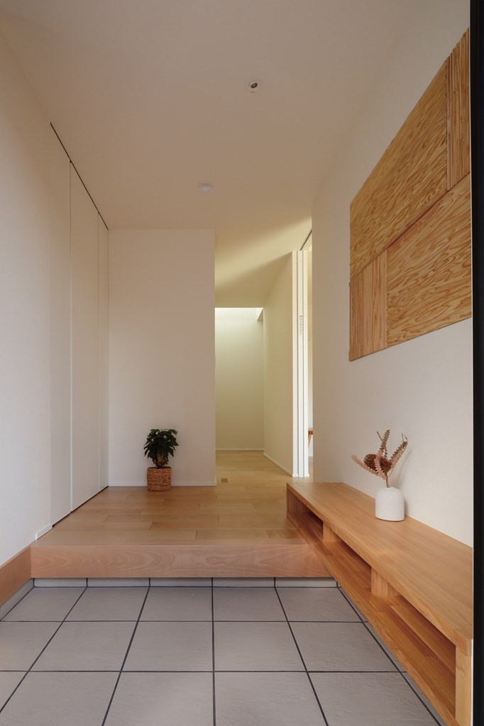 造作ベンチ収納を設えた玄関ホール。正面の中央廊下にはトップライトを設け、自然光を採り込む。