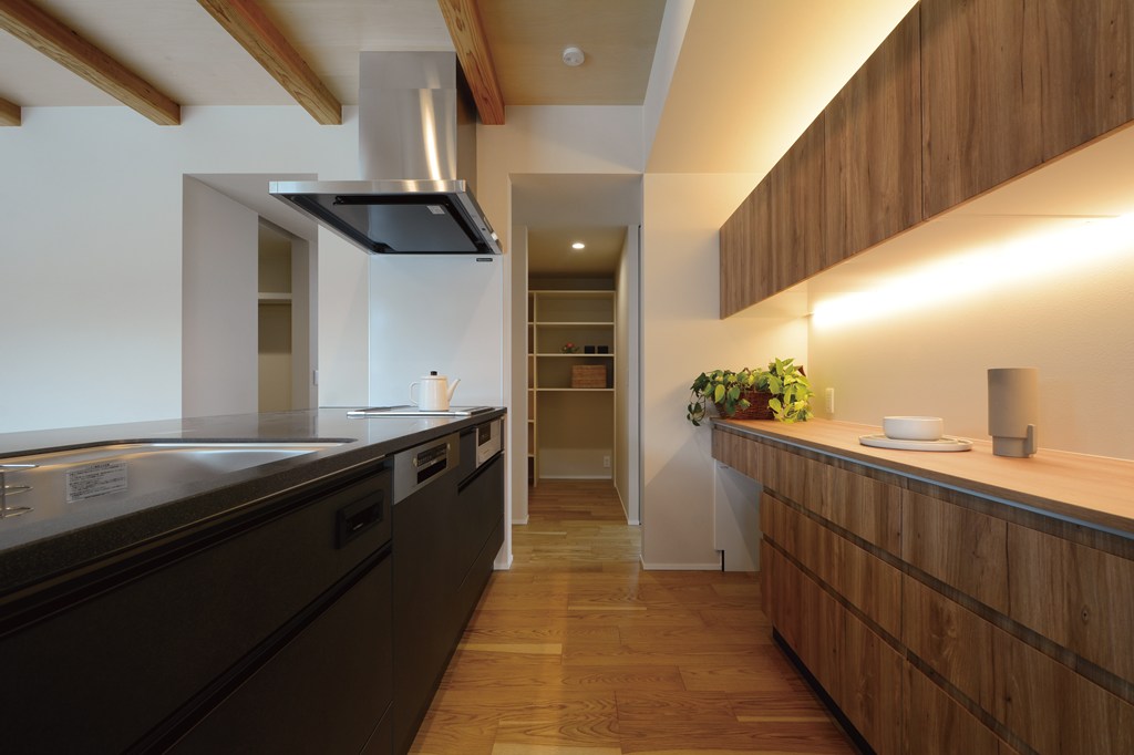 カップボードの吊戸棚に設けた間接照明で豊かな表情を持たせたキッチン収納。奥には大容量パントリーやファミリークロゼットへのスムーズな動線を実現。