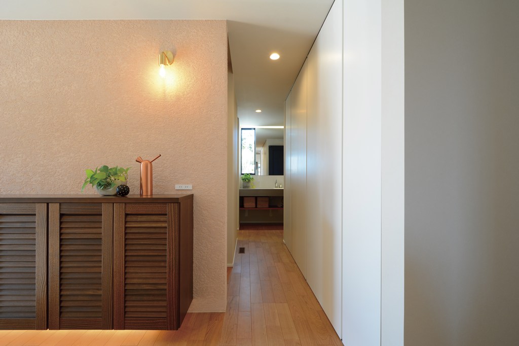 上質感のある塗り壁仕上げを採用した玄関ホールとシューズクロークの仕切り壁。真鍮のブラケットライトの穏やかな灯りで照らす。シューズクロークから水回りへのスムーズな動線で、使い勝手の良いデイリーユースを実現。